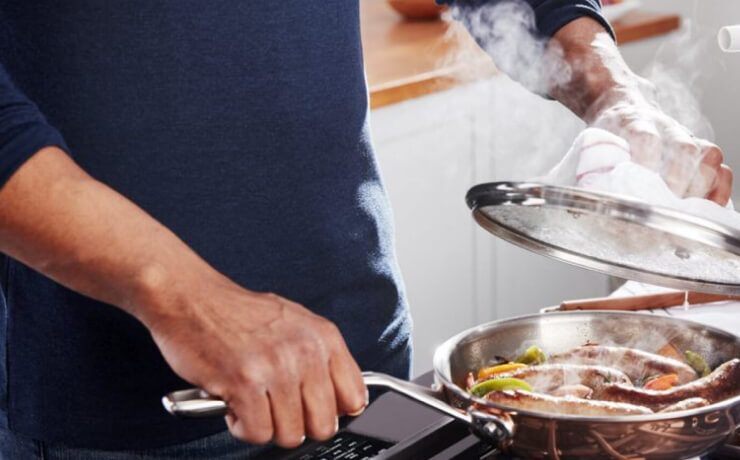 一名男子在炉子上用不锈钢锅炖着多汁的德国香肠，里面有sautéed的蔬菜。＂class=
